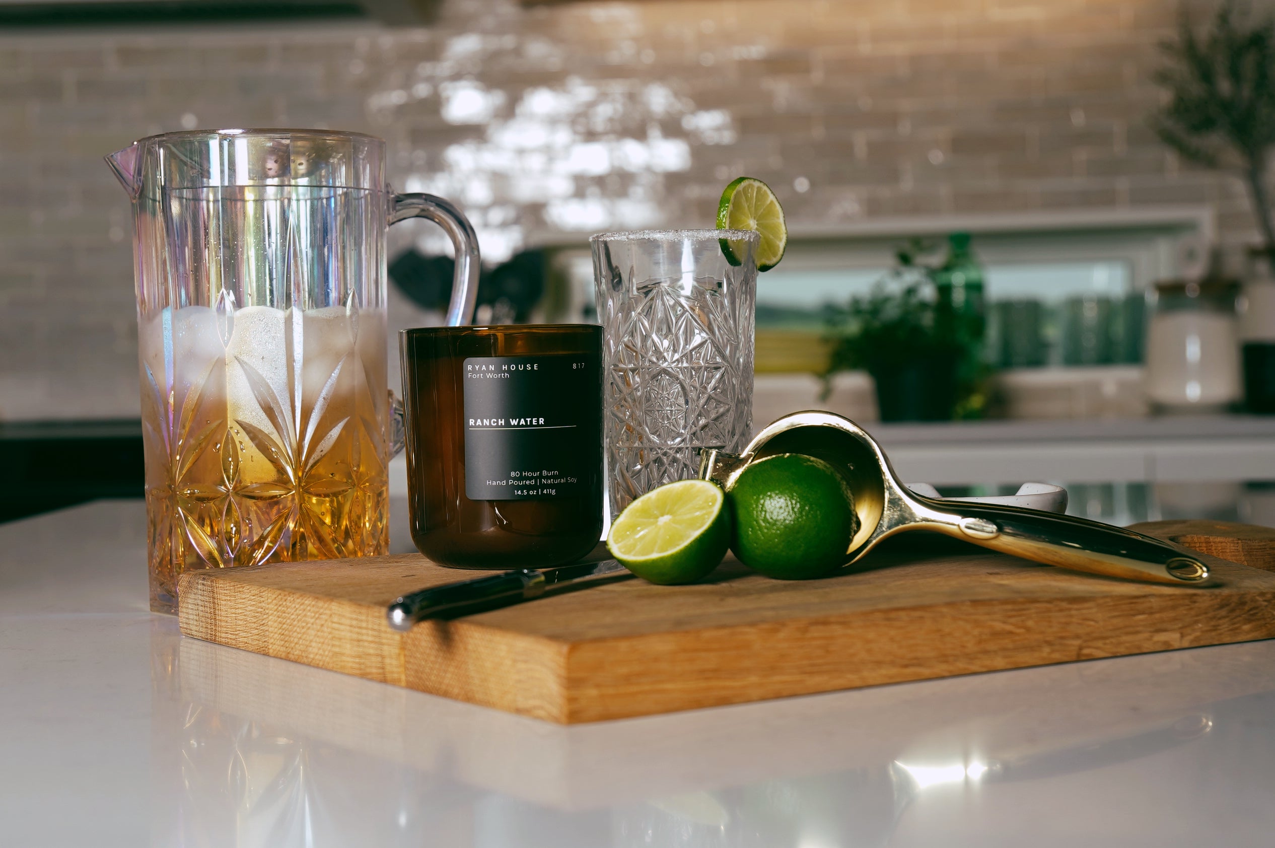 Cocktail setup with a glass, lime, and spoon on a cutting board in a kitchen.